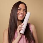 Frau hält die Flasche BREEZE Hitzschutz Spray von GLYNT in der Hand und lächelt. Das Haar ist geglättet, glänzend und frei von Frizz, sichtbar gepflegt und gesund