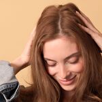 Frau mit gesund aussehendem, voluminösem Haar greift in den Ansatz, sichtbar frische Haarstruktur nach Anwendung von Trockenshampoo Schaum für mehr Fülle ohne Waschen