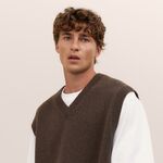Mann mit kurzen, lockigen, braunen Haaren und natürlichem Styling, trägt weißen Pullover mit braunem Strickwesten – Beispiel für Lockenstyling bei Männern