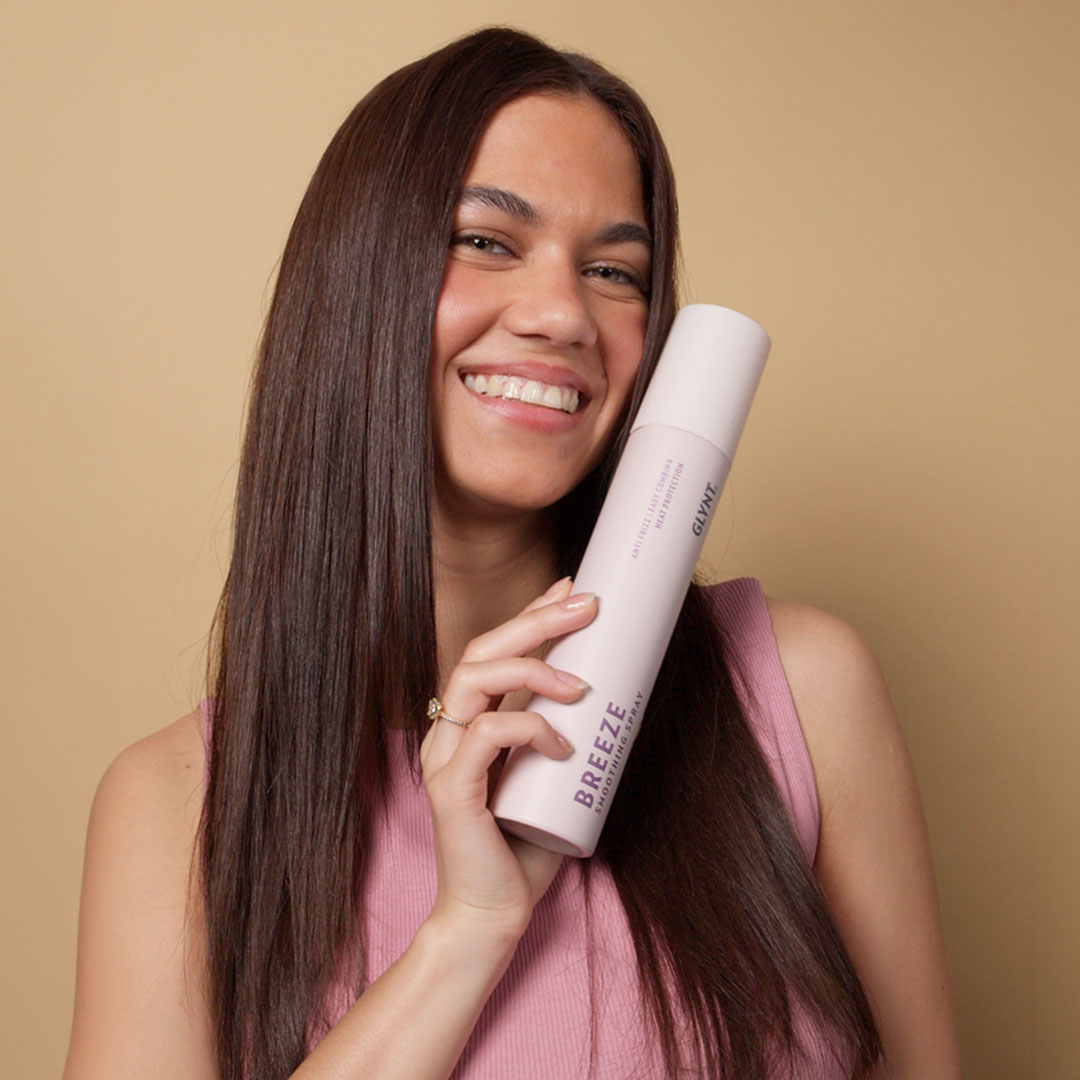 Frau hält die Flasche BREEZE Hitzschutz Spray von GLYNT in der Hand und lächelt. Das Haar ist geglättet, glänzend und frei von Frizz, sichtbar gepflegt und gesund