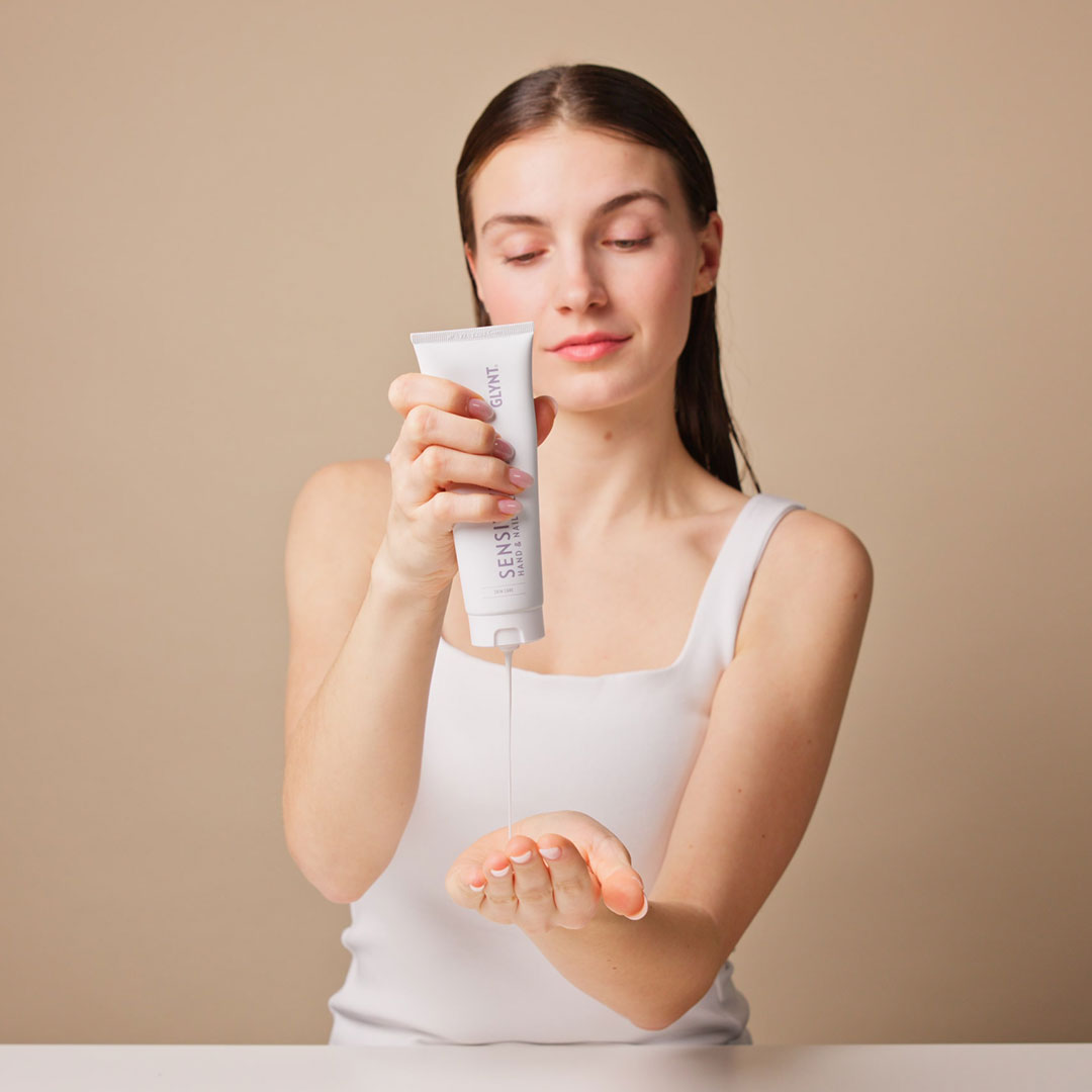 Frau gibt eine Handcreme für trockene Haut aus der Tube in die Hand – Anwendung des SENSITIVE Hand & Nail Balm.