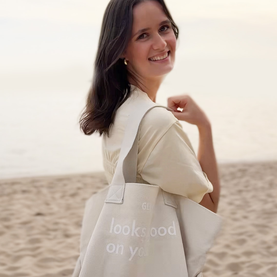 Frau am Strand mit beiger GLYNT Stofftasche „looks good on you“ über der Schulter.